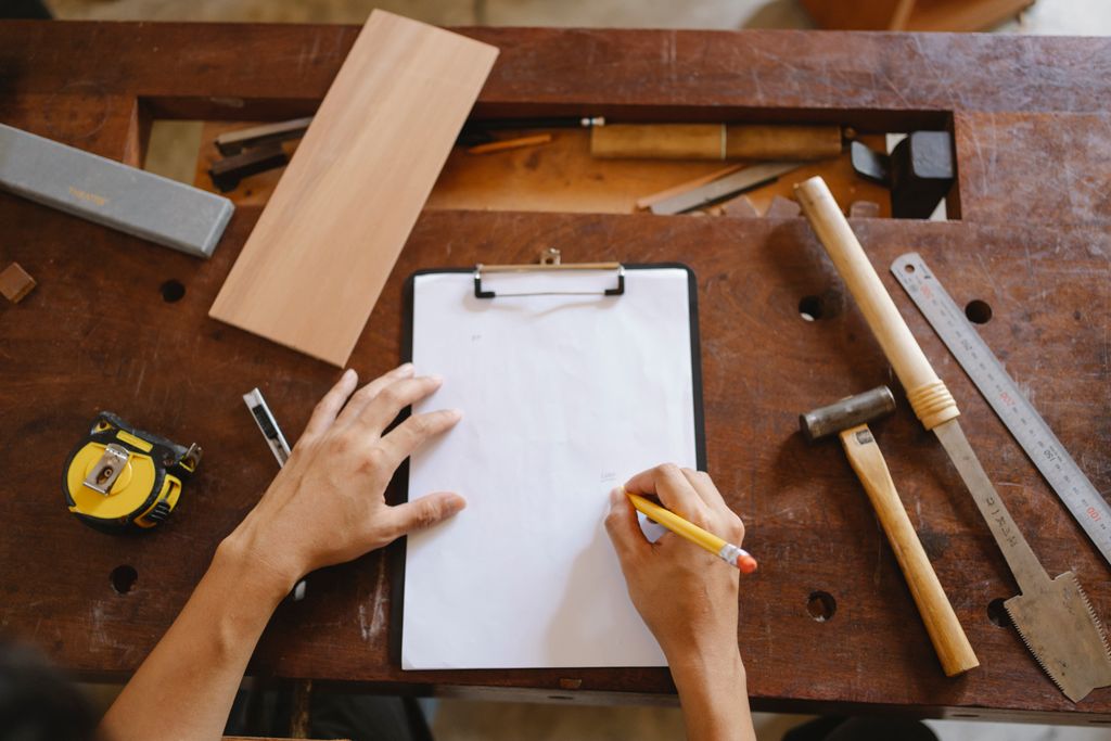 From above of crop faceless man holding pencil and paper while sitting at wooden table with instruments